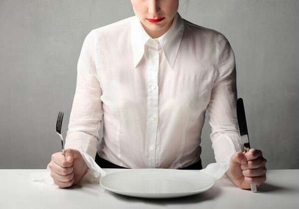 Девушка сидит за столом с тарелкой, ножом и вилкой